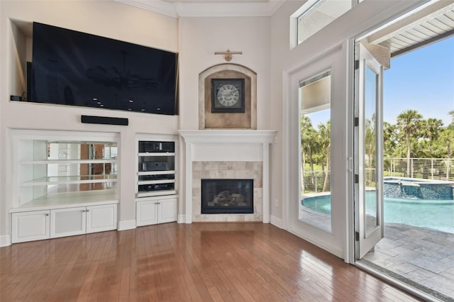 unfurnished living room featuring a towering ceiling, crown molding, a fireplace, baseboards, and wood-type flooring