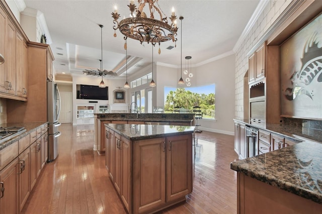 kitchen with an inviting chandelier, wood-type flooring, a large island with sink, a sink, and stainless steel appliances