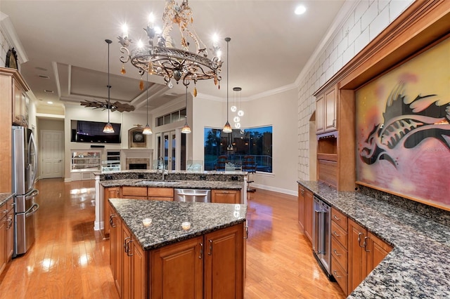 kitchen featuring appliances with stainless steel finishes, a sink, brown cabinetry, light wood-style flooring, and a large island with sink