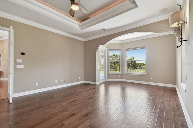 empty room featuring crown molding, dark wood-style flooring, ceiling fan, a raised ceiling, and arched walkways