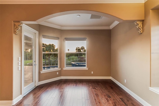 empty room featuring dark wood-style flooring, arched walkways, baseboards, and crown molding