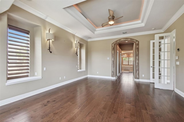 empty room featuring ornamental molding, ceiling fan, a tray ceiling, hardwood / wood-style flooring, and arched walkways