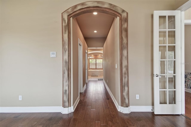corridor with arched walkways, baseboards, and dark wood finished floors