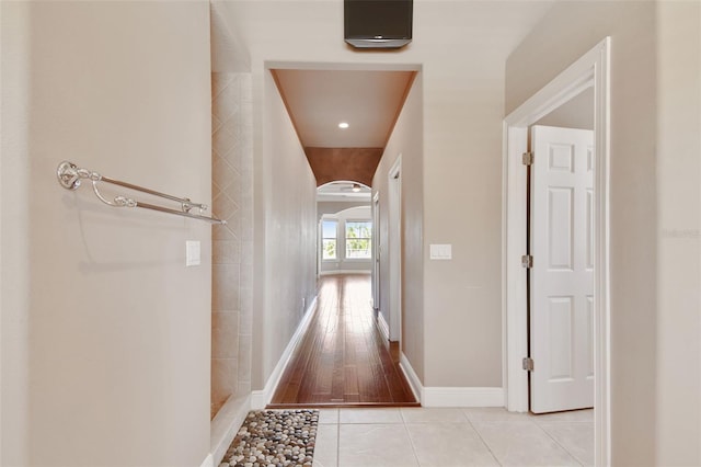 hallway with arched walkways, baseboards, and light tile patterned floors