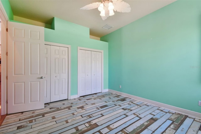 unfurnished bedroom featuring multiple closets, baseboards, a ceiling fan, and visible vents