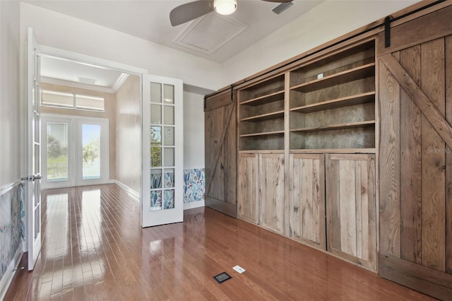 interior space with visible vents, hardwood / wood-style floors, baseboards, a barn door, and french doors