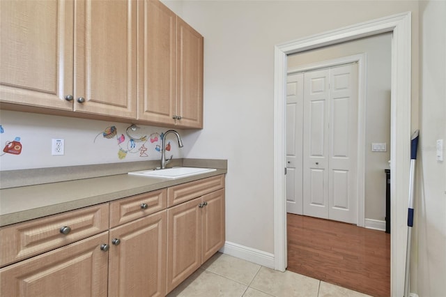 kitchen featuring baseboards, a sink, light tile patterned flooring, and light brown cabinets