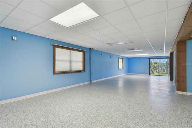 spare room featuring baseboards, a drop ceiling, and speckled floor