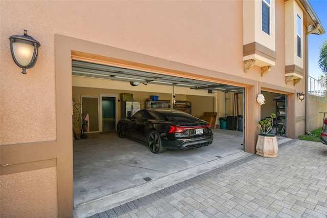 garage featuring decorative driveway, a garage door opener, and stainless steel refrigerator with ice dispenser