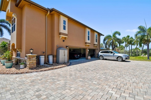 view of side of property with decorative driveway, a garage, and stucco siding