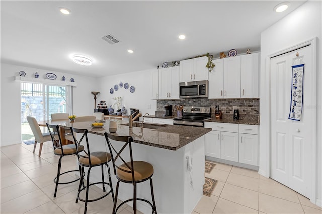 kitchen featuring a sink, stainless steel appliances, a kitchen bar, backsplash, and a center island with sink