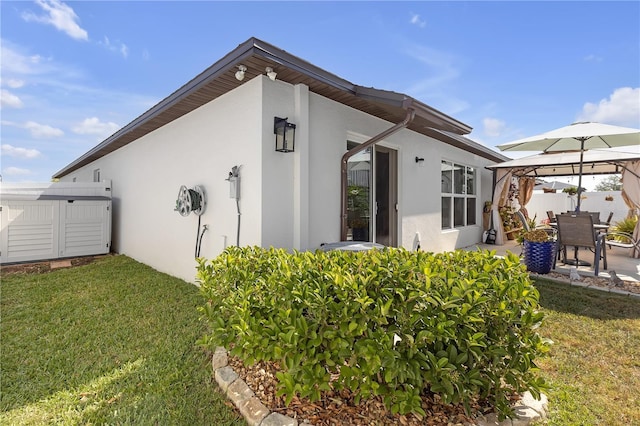 view of property exterior featuring a gazebo, a lawn, stucco siding, and fence