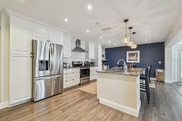 13749 80th Ave, Seminole, FL 33776 - kitchen featuring wall chimney range hood, appliances with stainless steel finishes, a sink, visible vents, and a center island with sink