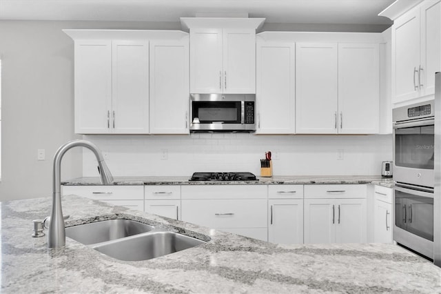 kitchen with a sink, appliances with stainless steel finishes, decorative backsplash, and white cabinetry
