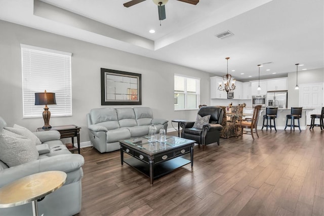 living room featuring baseboards, visible vents, ceiling fan with notable chandelier, and dark wood-type flooring