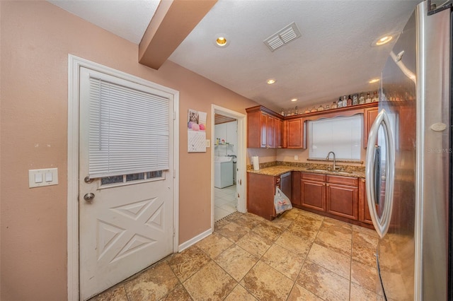 kitchen featuring light stone counters, a sink, freestanding refrigerator, washer / clothes dryer, and visible vents