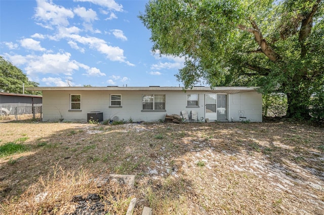 back of house featuring central AC unit, concrete block siding, and fence