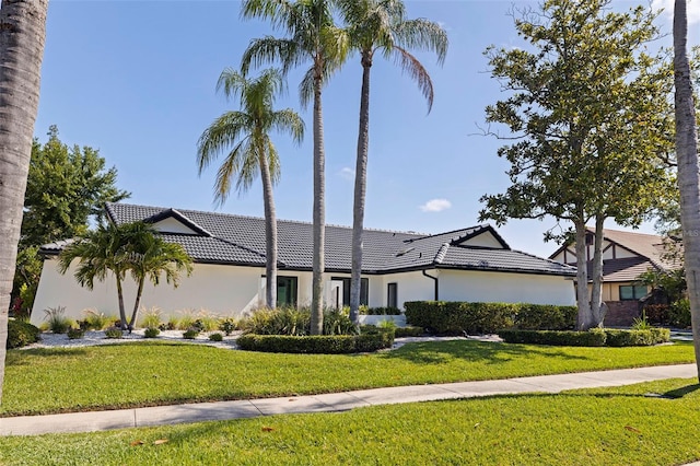 ranch-style house with a tile roof, a front yard, and stucco siding