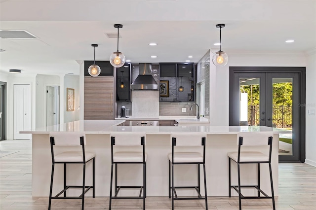 kitchen featuring visible vents, decorative backsplash, wall chimney range hood, light countertops, and a sink