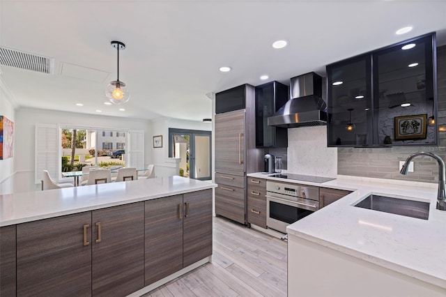 kitchen with wall chimney range hood, visible vents, black electric cooktop, a sink, and oven