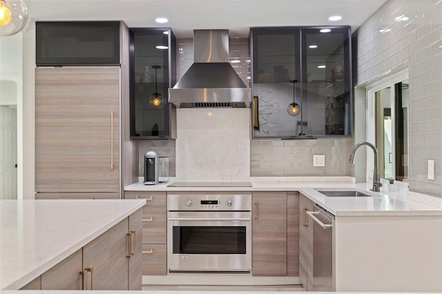 kitchen with light stone countertops, appliances with stainless steel finishes, a sink, wall chimney exhaust hood, and backsplash