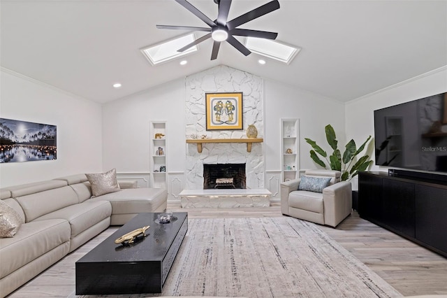 living room with vaulted ceiling with skylight, built in features, a ceiling fan, wood finished floors, and a high end fireplace