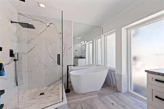 full bathroom with crown molding, a freestanding bath, vanity, a marble finish shower, and wood finished floors