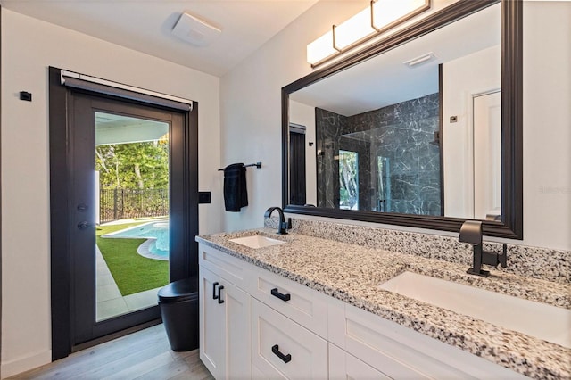 full bath featuring double vanity, a sink, a marble finish shower, and wood finished floors