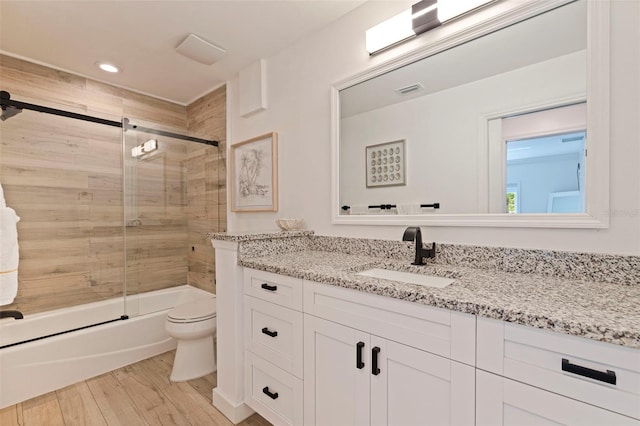 bathroom featuring vanity, wood finished floors, toilet, recessed lighting, and bath / shower combo with glass door