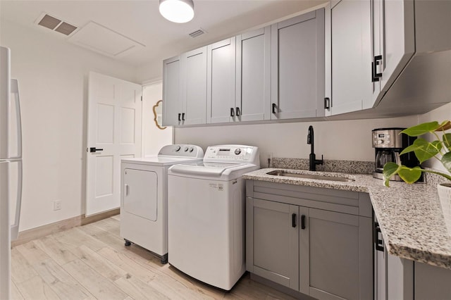 clothes washing area featuring visible vents, a sink, light wood finished floors, and separate washer and dryer