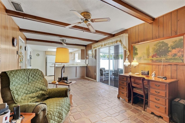 interior space featuring visible vents, wood walls, beamed ceiling, a textured ceiling, and a ceiling fan