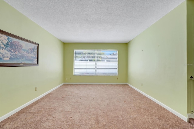empty room with light colored carpet, a textured ceiling, and baseboards