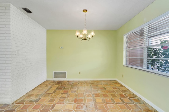 empty room featuring a chandelier, brick wall, visible vents, and baseboards