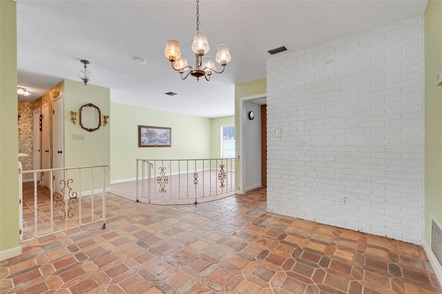 unfurnished room with visible vents, brick wall, baseboards, stone finish floor, and a chandelier