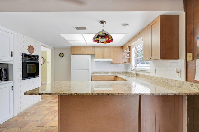 kitchen featuring light stone counters, a sink, a peninsula, under cabinet range hood, and black appliances