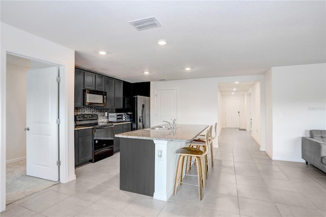 kitchen featuring light tile patterned floors, visible vents, a kitchen breakfast bar, black appliances, and a kitchen island with sink