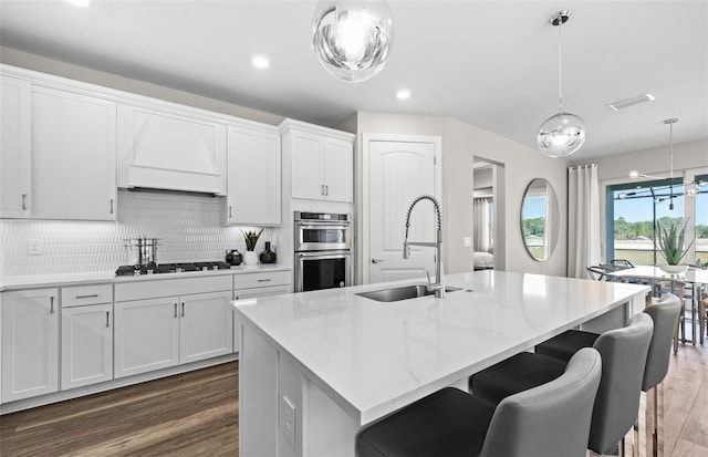 kitchen with double oven, dark wood-style flooring, a sink, visible vents, and premium range hood