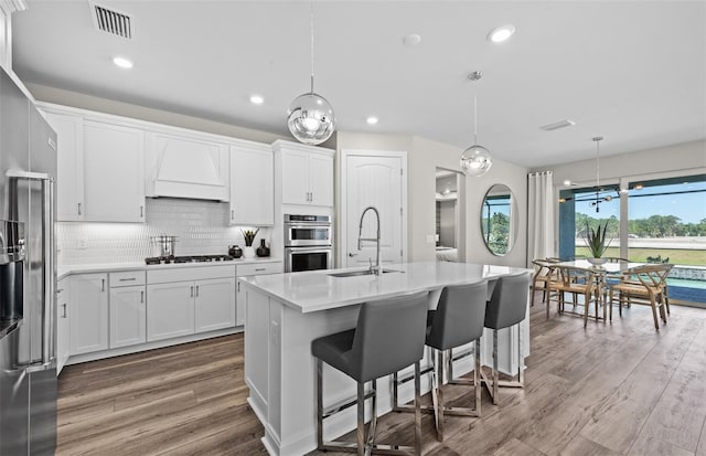 kitchen with a sink, custom exhaust hood, gas cooktop, double oven, and wood finished floors