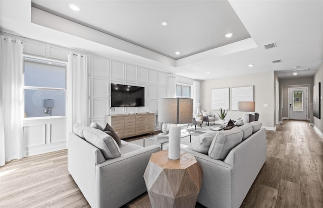 living area with recessed lighting, a decorative wall, light wood-type flooring, visible vents, and a raised ceiling