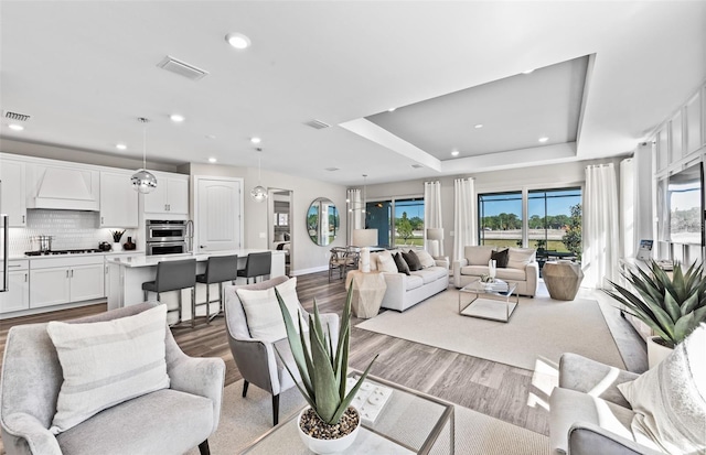 living room with visible vents, wood finished floors, a raised ceiling, and recessed lighting