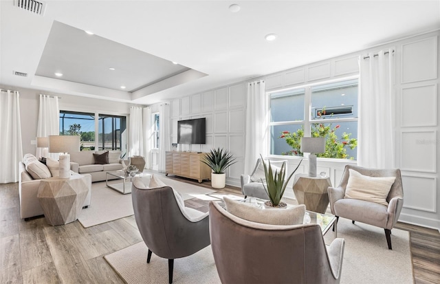 living area with visible vents, a decorative wall, light wood finished floors, and a tray ceiling