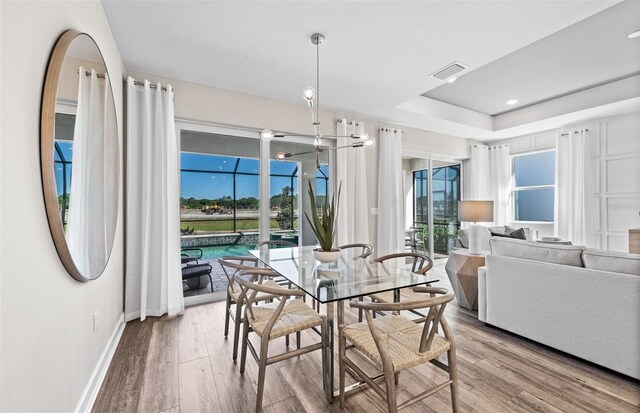 dining area with baseboards, wood finished floors, visible vents, and a raised ceiling