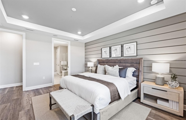bedroom with recessed lighting, baseboards, wood finished floors, and a tray ceiling