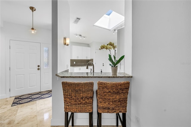 kitchen featuring visible vents, decorative backsplash, white cabinetry, stone counters, and a skylight