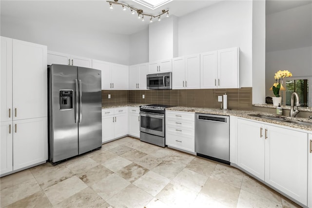 kitchen with backsplash, a towering ceiling, light stone counters, white cabinets, and stainless steel appliances