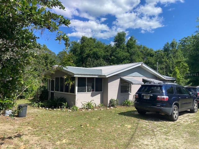 view of front facade featuring a front lawn, metal roof, concrete block siding, and a sunroom