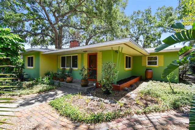 ranch-style home featuring stucco siding, covered porch, and a chimney