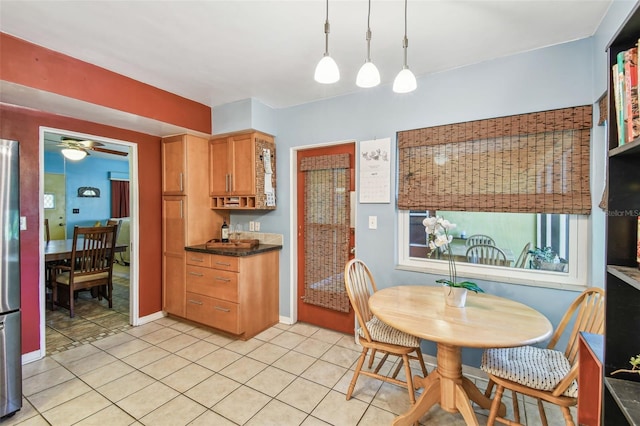 kitchen with light tile patterned floors, dark countertops, ceiling fan, freestanding refrigerator, and decorative light fixtures