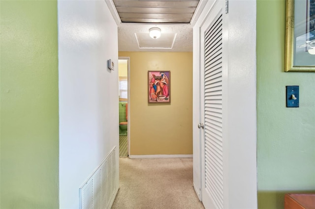 hall featuring baseboards, visible vents, attic access, and carpet