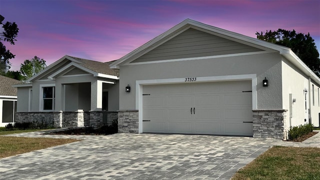 view of front of property featuring decorative driveway, stone siding, stucco siding, and a garage